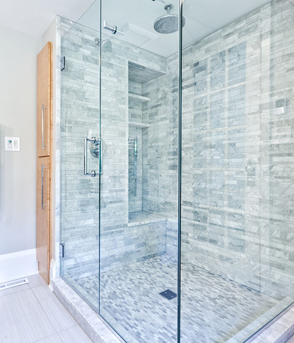 Contemporary interior bathroom design with glass enclosed shower stall with Cararra marble tiles